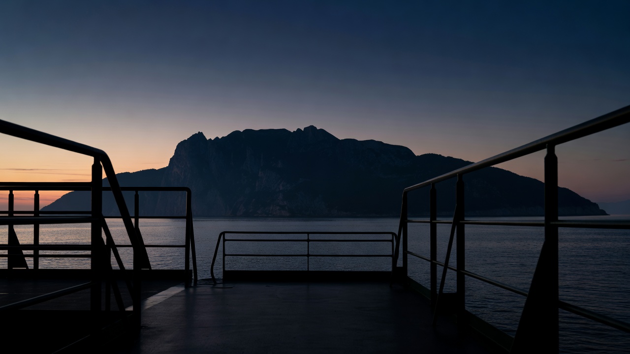 Ferry railings in silhouette as a mountainous island darkens at dusk